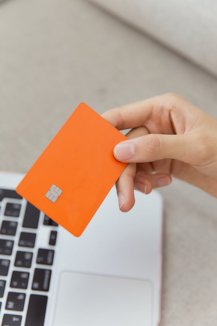 Close-up shot of an orange credit card held above a laptop, emphasizing digital payment.